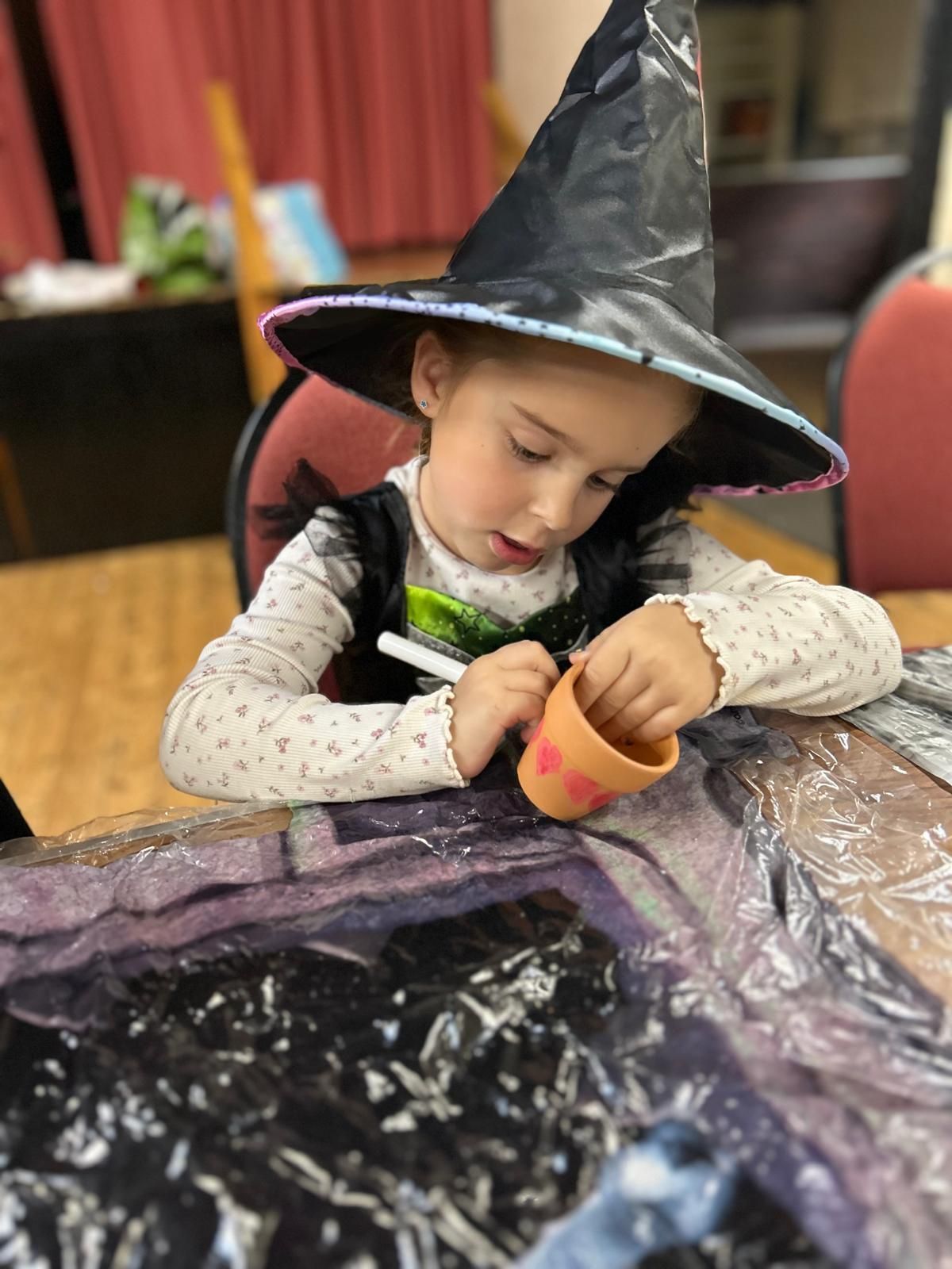 A little girl wearing a witch hat is sitting at a table for Dragonfly crafts party