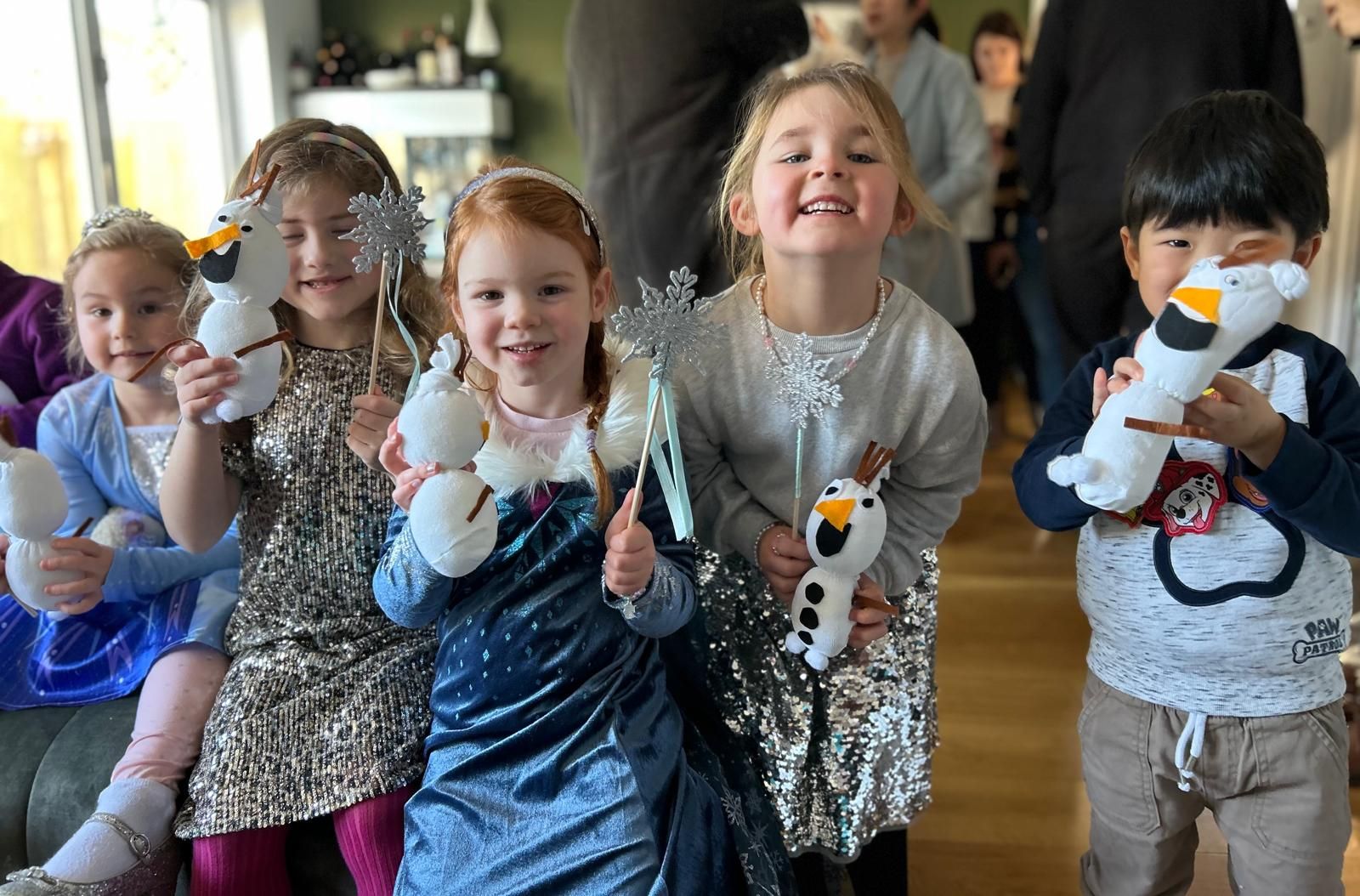 A group of children are posing for a picture while holding stuffed snowmen at Dragonfly-craft parties.