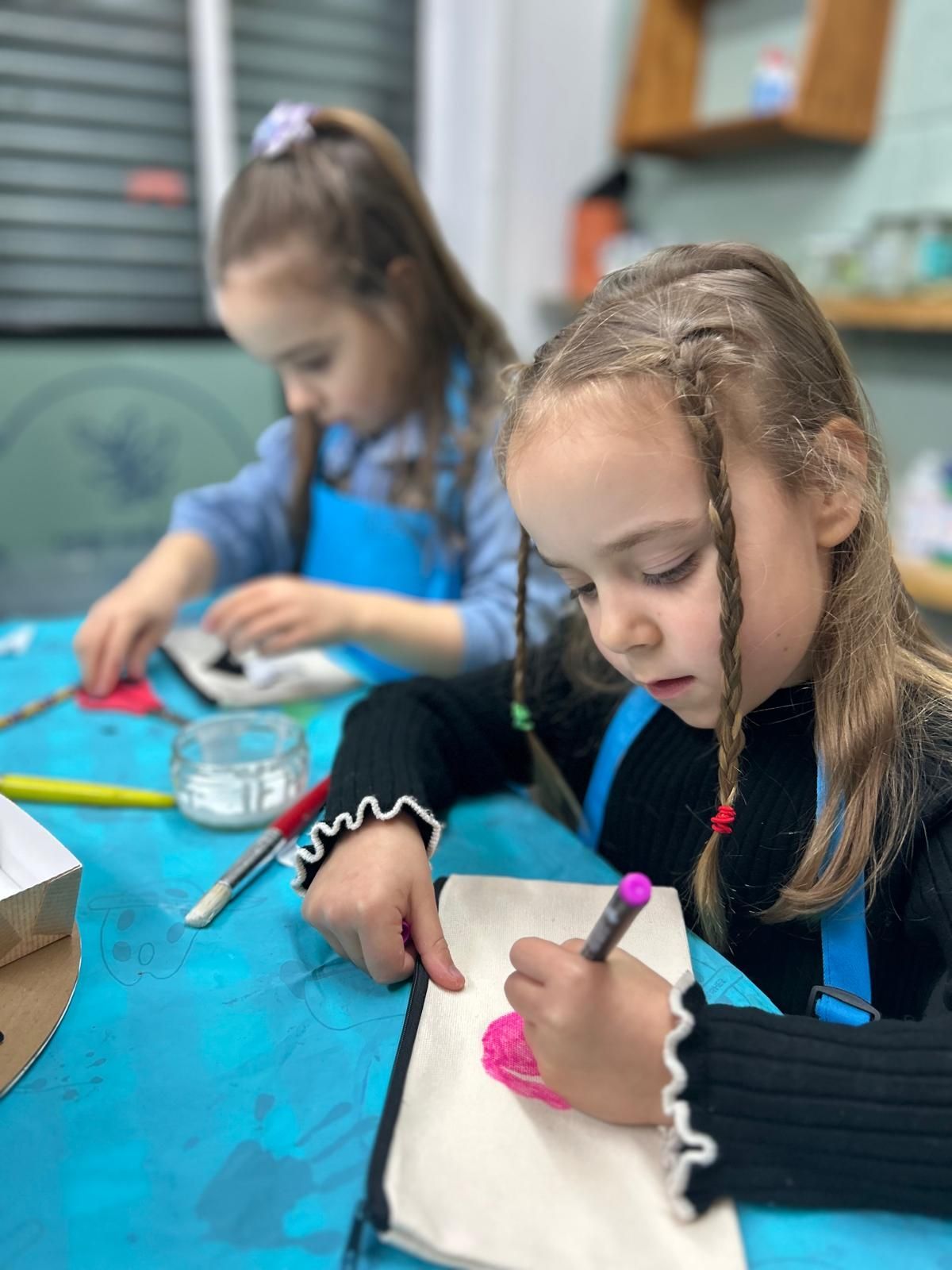 Two little girls are sitting at a table drawing on a piece of paper at Dragonfly-craft parties.