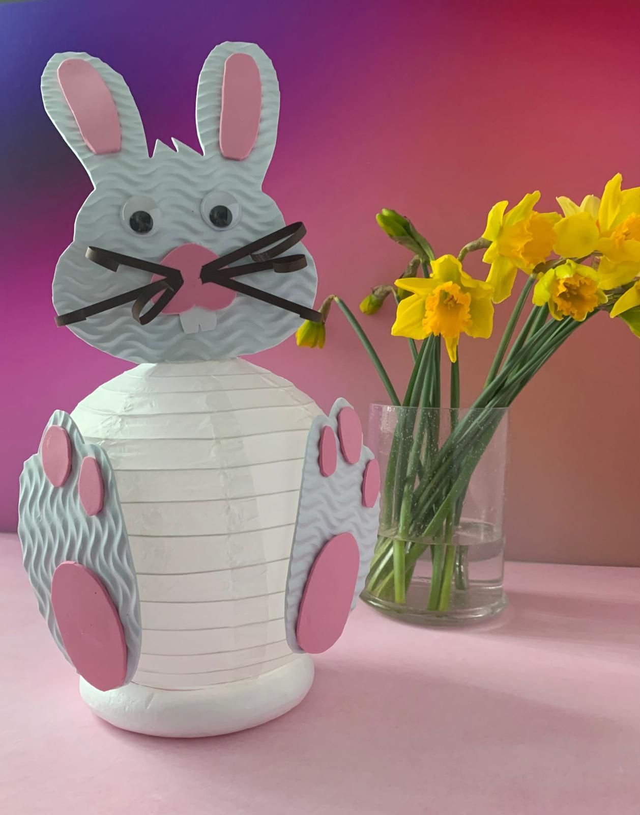 A paper bunny is sitting next to a vase of yellow flowers for craft party