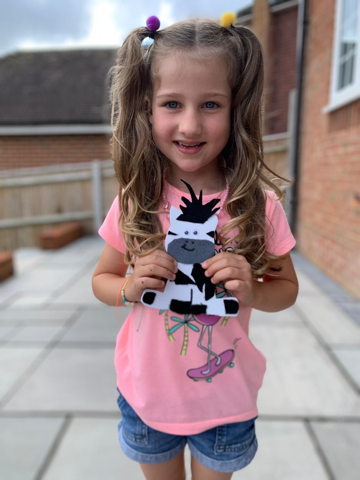 A little girl in a pink shirt is holding a paper zebra at Dragonfly craft party