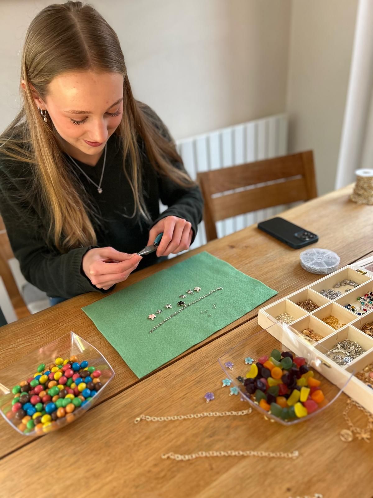 A woman is sitting at a table making a necklace with beads for charm party at Dragonfly crafts parties