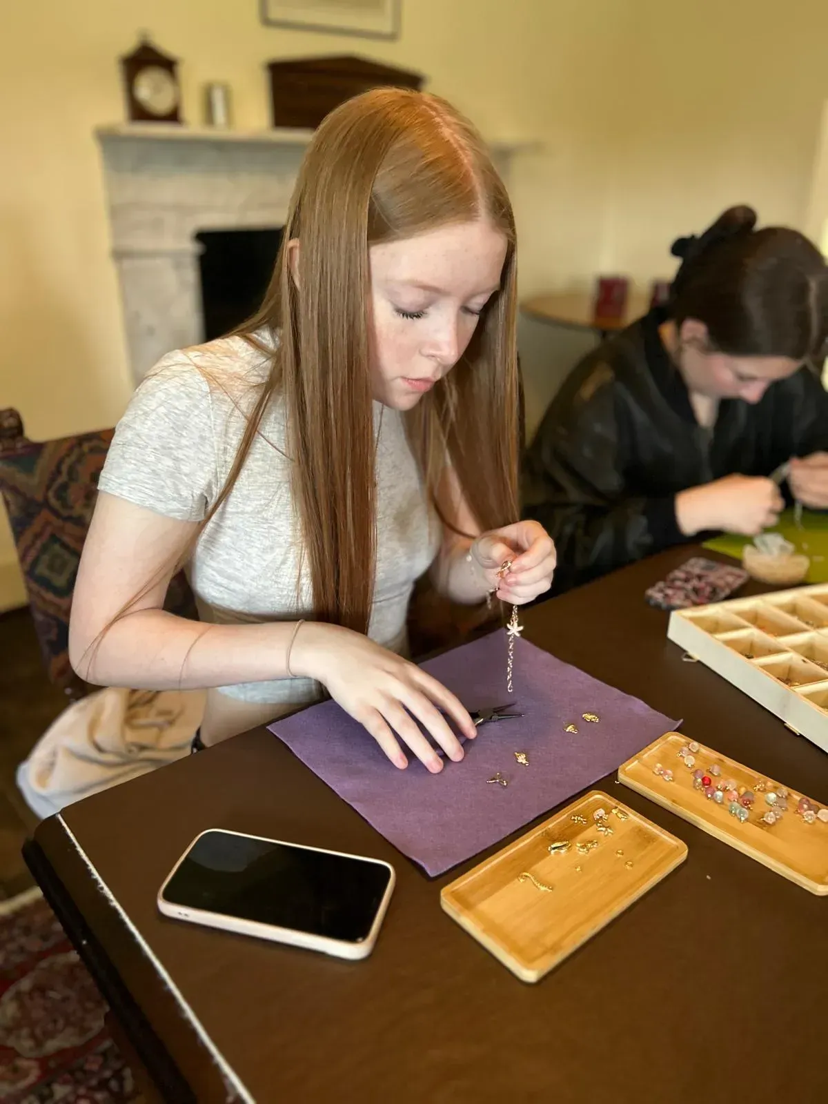 A woman is sitting at a table making a necklace with beads for charm party at Dragonfly crafts parties