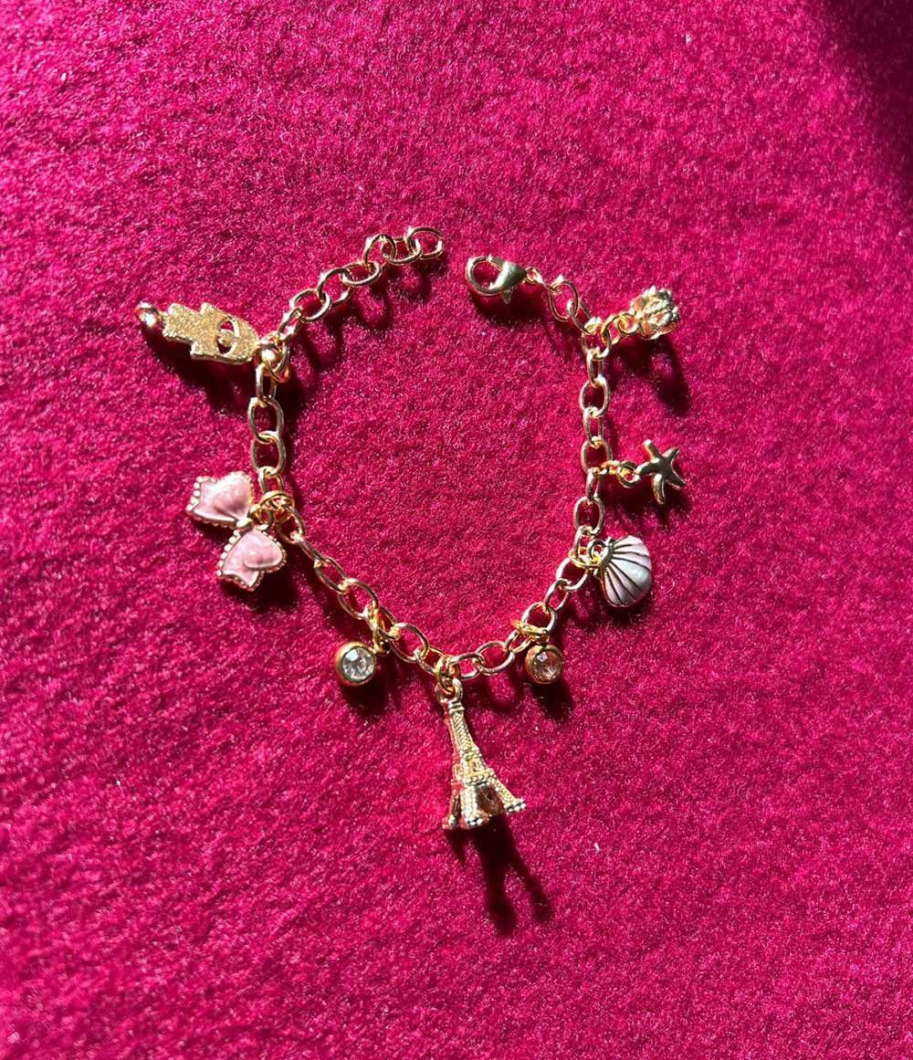 A gold bracelet with pink charms is sitting on a pink surface for charm party at Dragonfly crafts parties