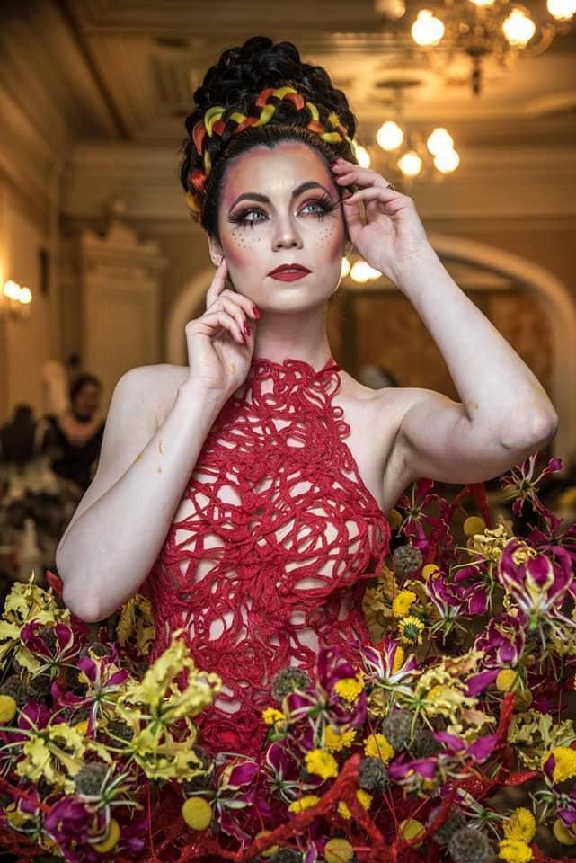 Una donna con un vestito rosso è circondata da fiori.