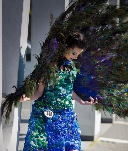 A woman in a peacock costume is standing next to a wall.