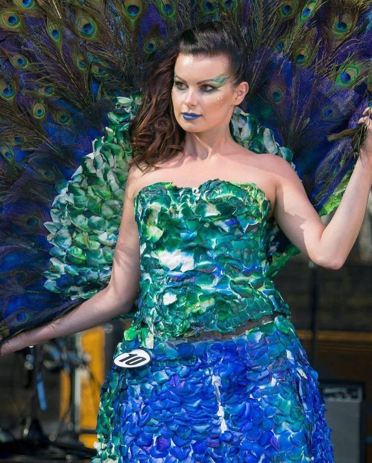 A woman in a peacock costume holds a peacock feather fan.