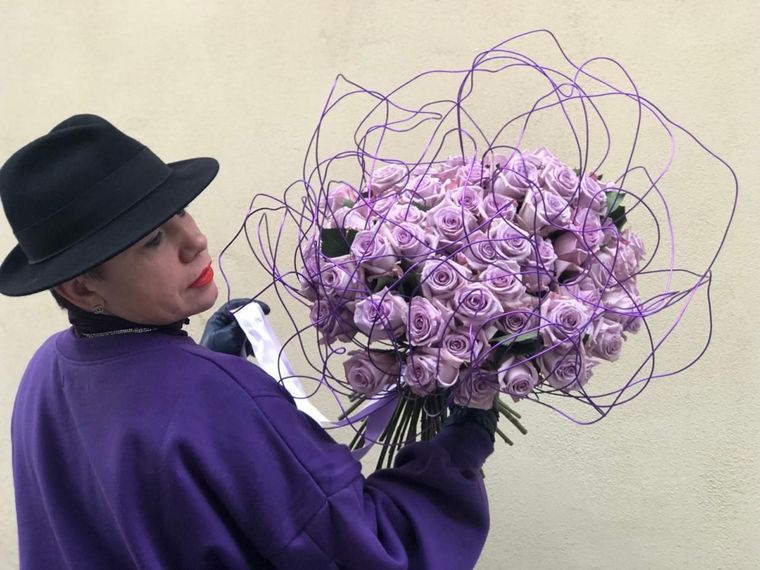 Un uomo con un cappello nero tiene in mano un grande mazzo di rose viola.