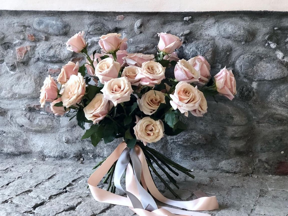 Un mazzo di rose rosa è appoggiato davanti a un muro di pietra.