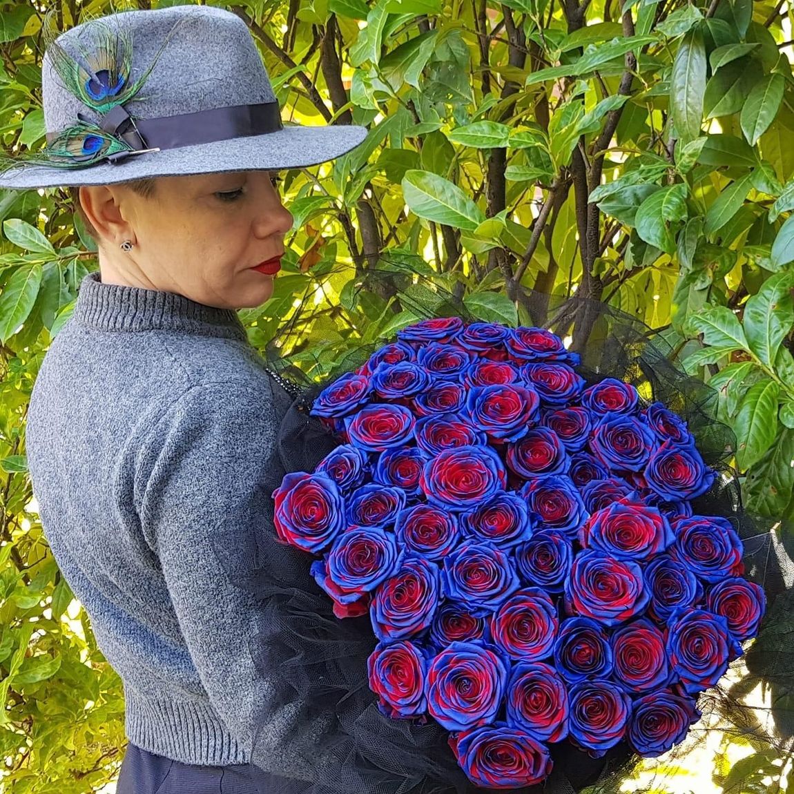 Una donna con un cappello tiene in mano un mazzo di rose blu e rosse.
