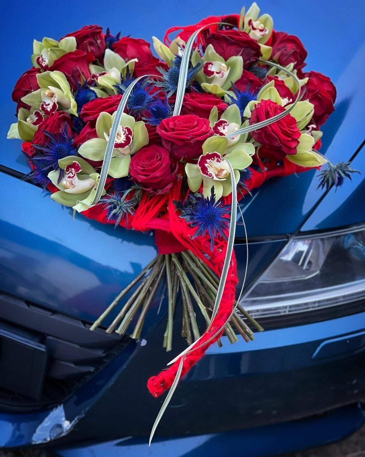 Un mazzo di rose rosse e orchidee verdi sul cofano di un'auto blu