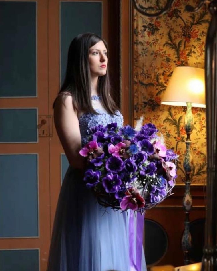 Una donna con un vestito blu tiene in mano un mazzo di fiori viola.