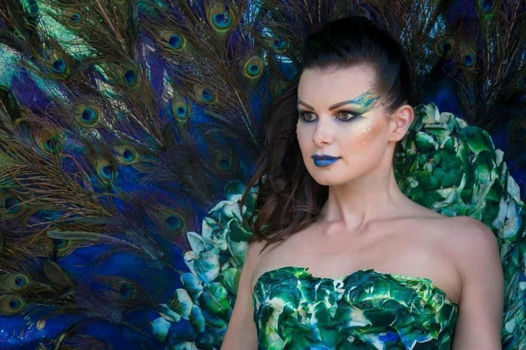 Una donna con piume di pavone dipinte sul viso è seduta davanti a un ventaglio di piume di pavone.