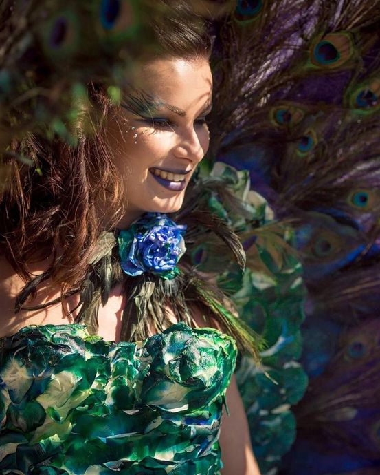 A woman in a peacock costume is standing in front of a peacock feather.