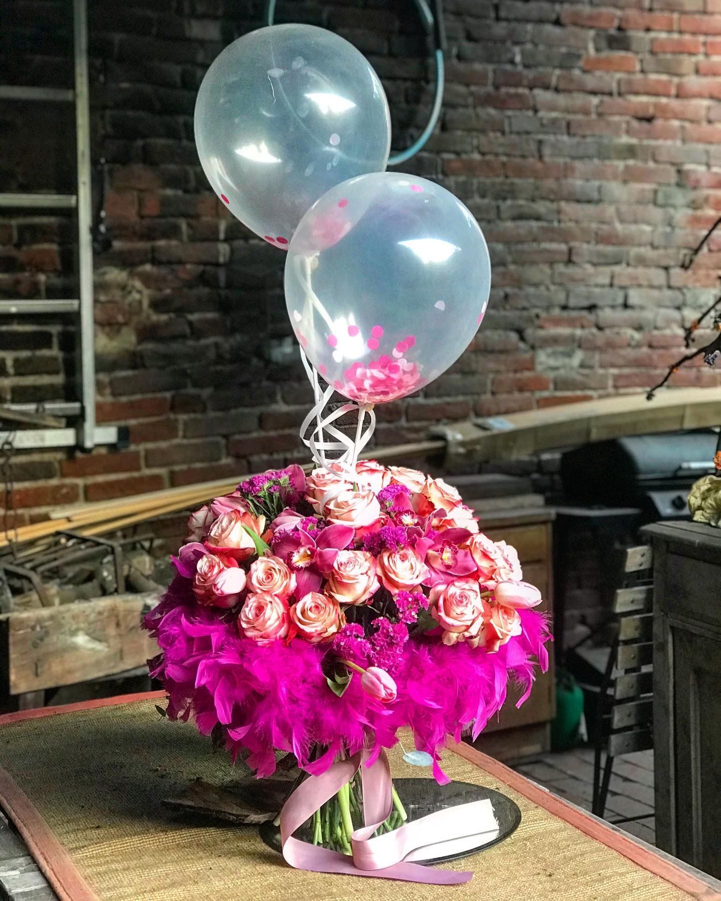 Un vaso pieno di fiori rosa e palloncini su un tavolo.