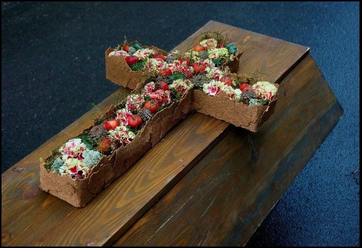 A wooden coffin with a cross made of flowers on top.