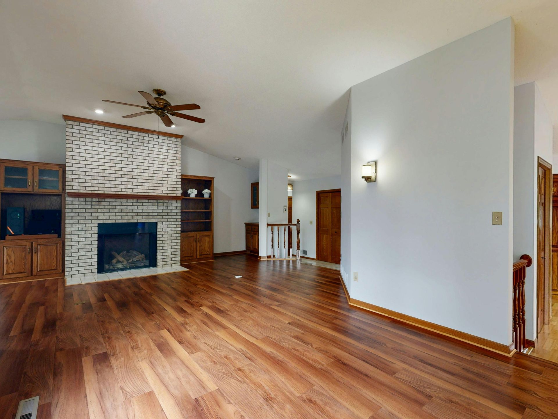 Spacious living room with hardwood floors, a stone fireplace, ceiling fan, and wall sconce lighting.