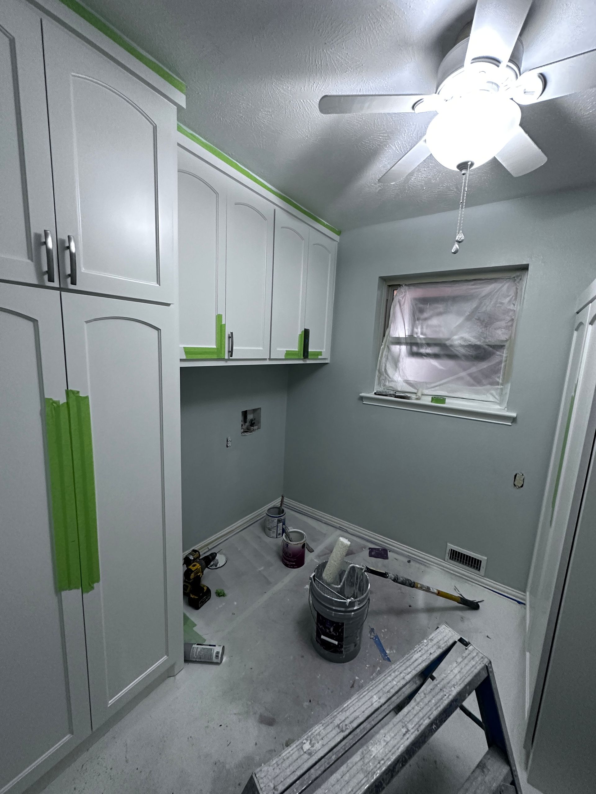 A room with a ceiling fan and a bucket of paint on the floor