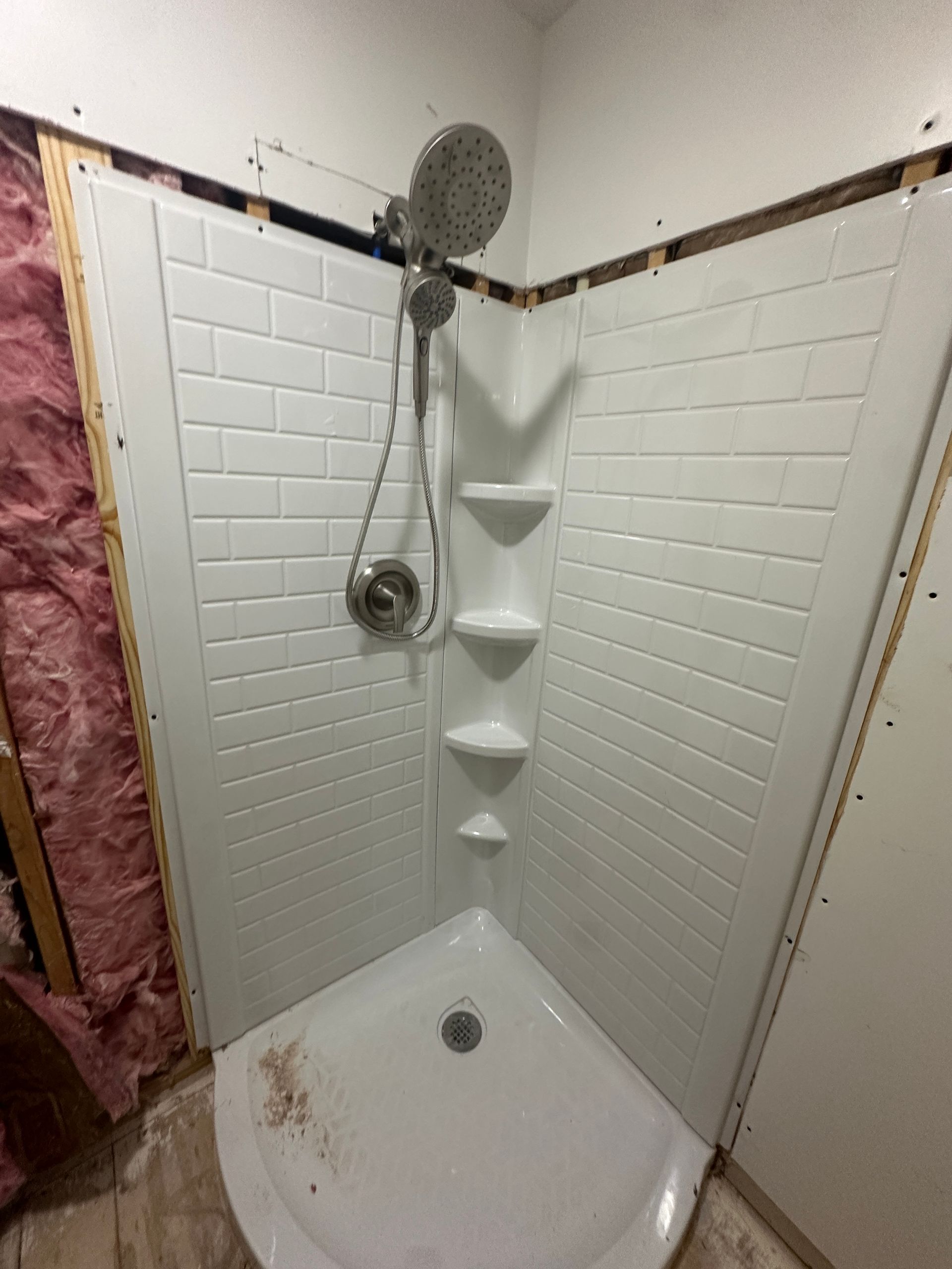 A shower stall with a shower head and shelves in a bathroom.