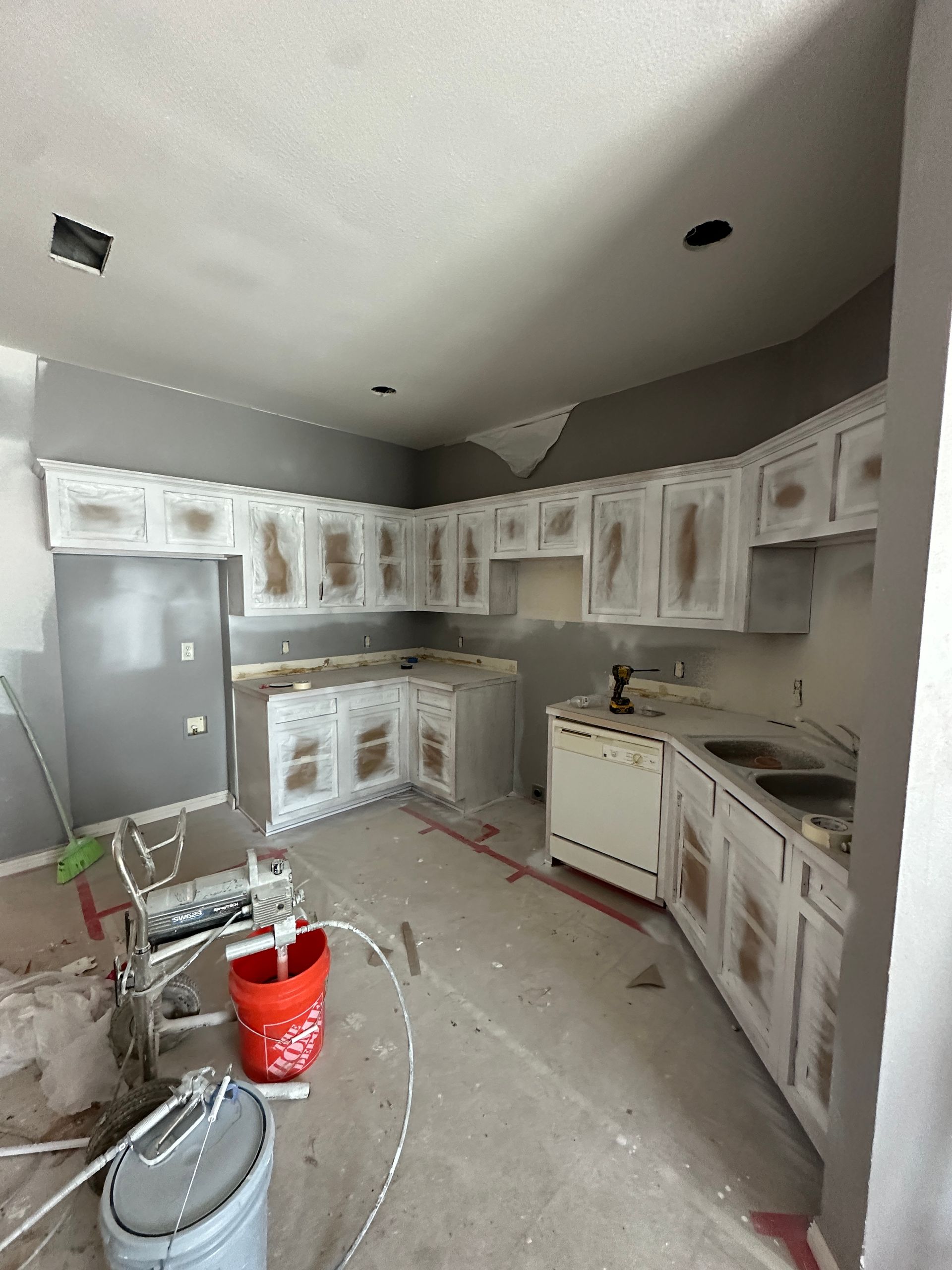 A kitchen under construction with white cabinets and a red bucket