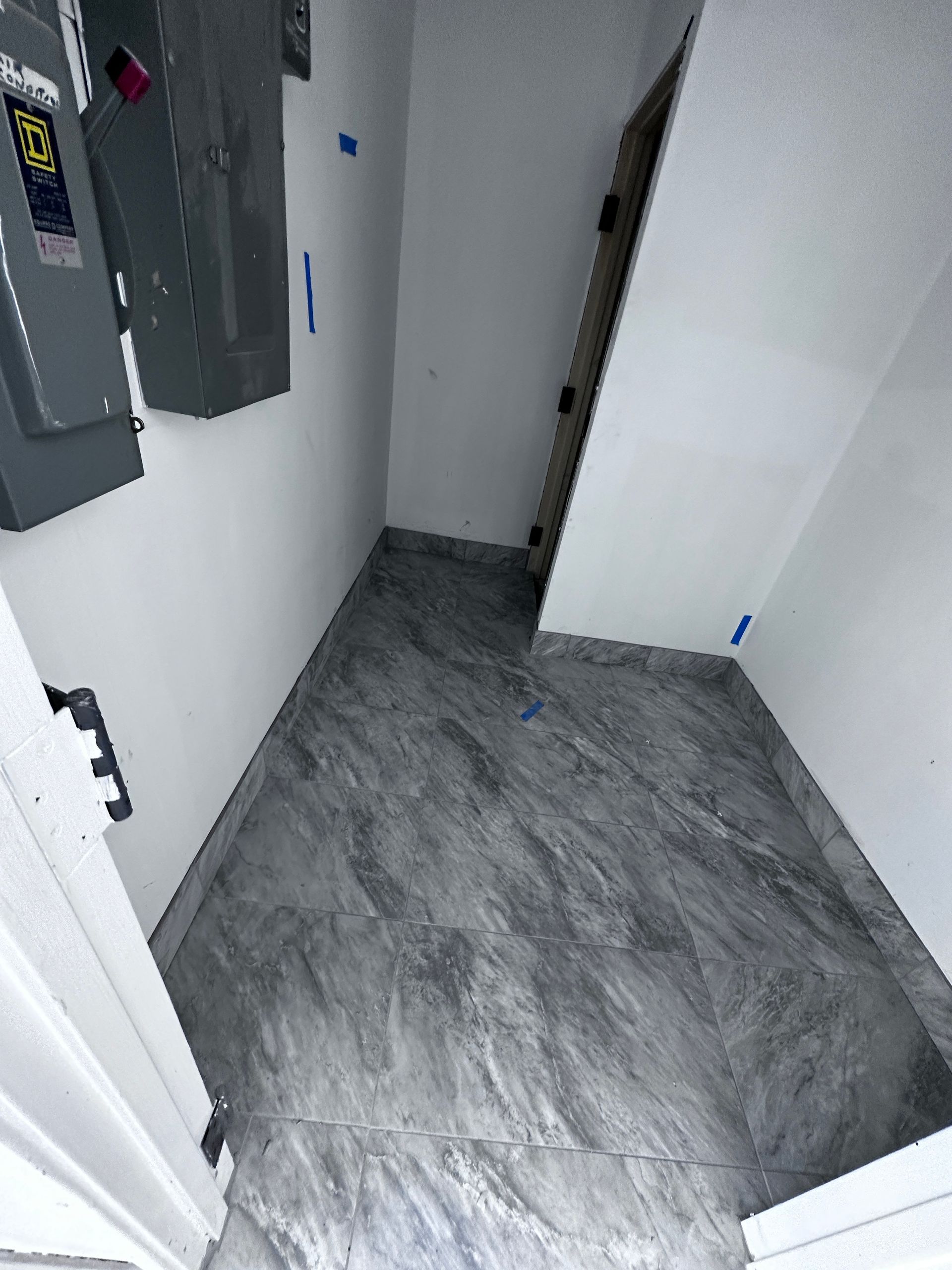 A room with a gray tile floor and a black box on the wall.