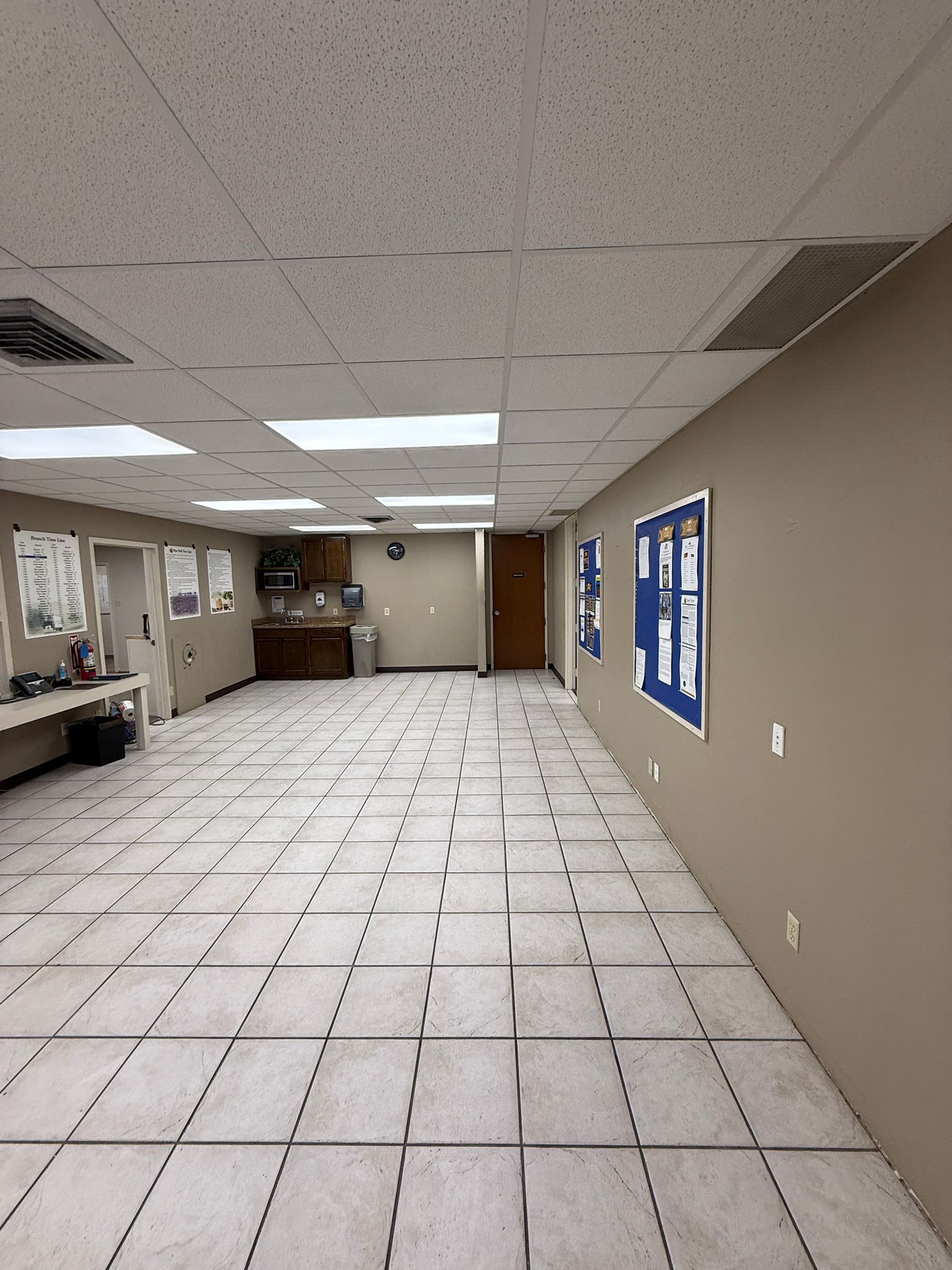 A large room with a tiled floor and a bulletin board on the wall.