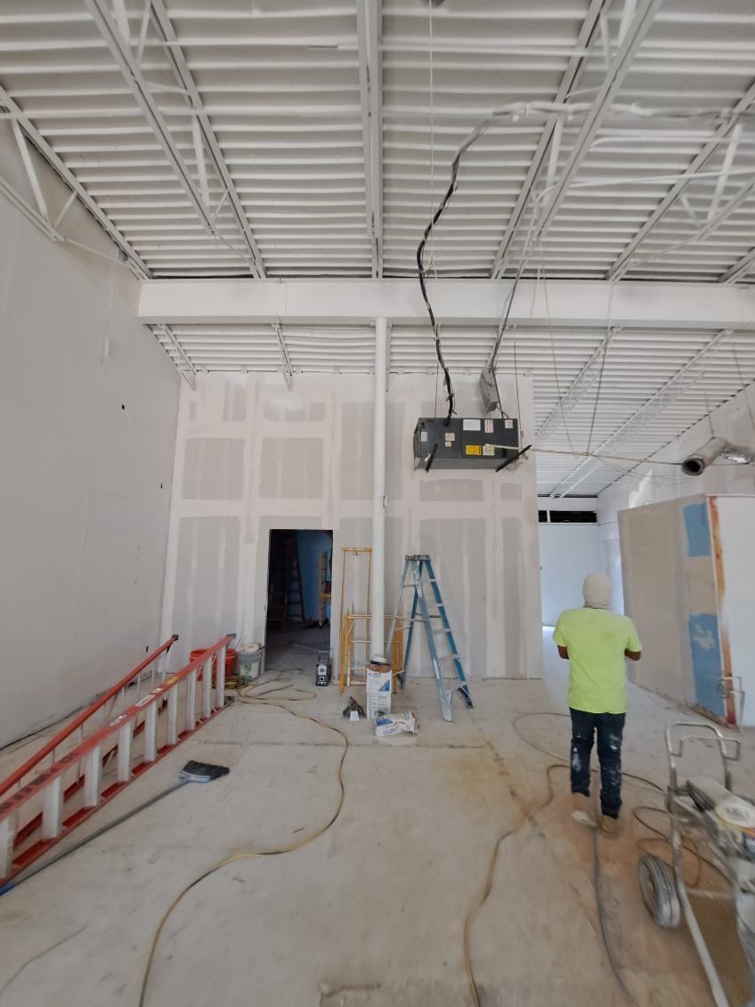 A man in a green shirt is standing in an empty room with a ladder.