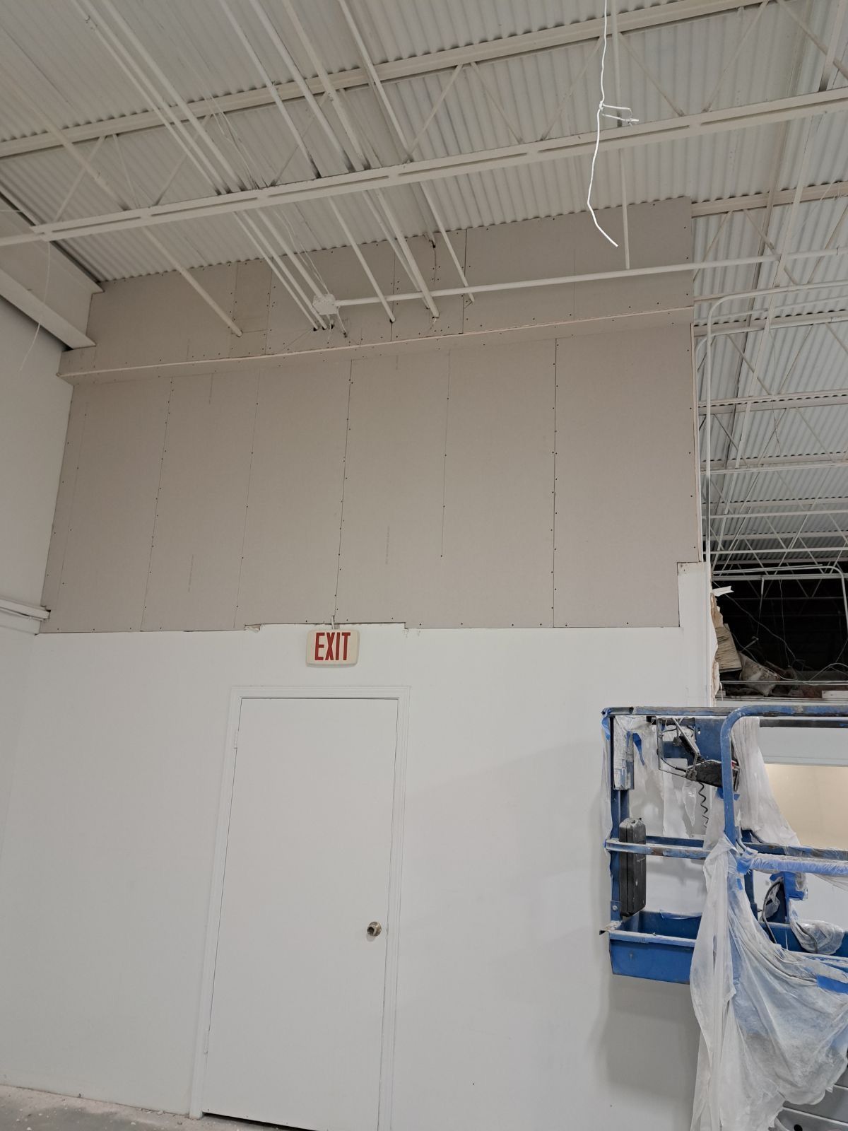 A white wall with a red exit sign on it in a building under construction.