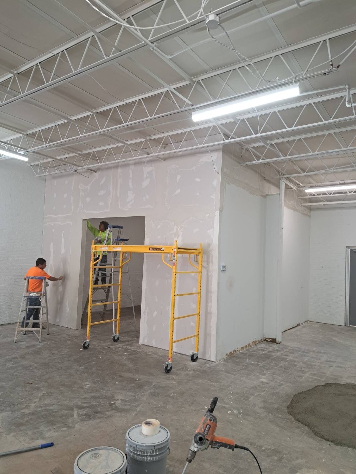 A man is painting a wall in a room with a scaffolding.