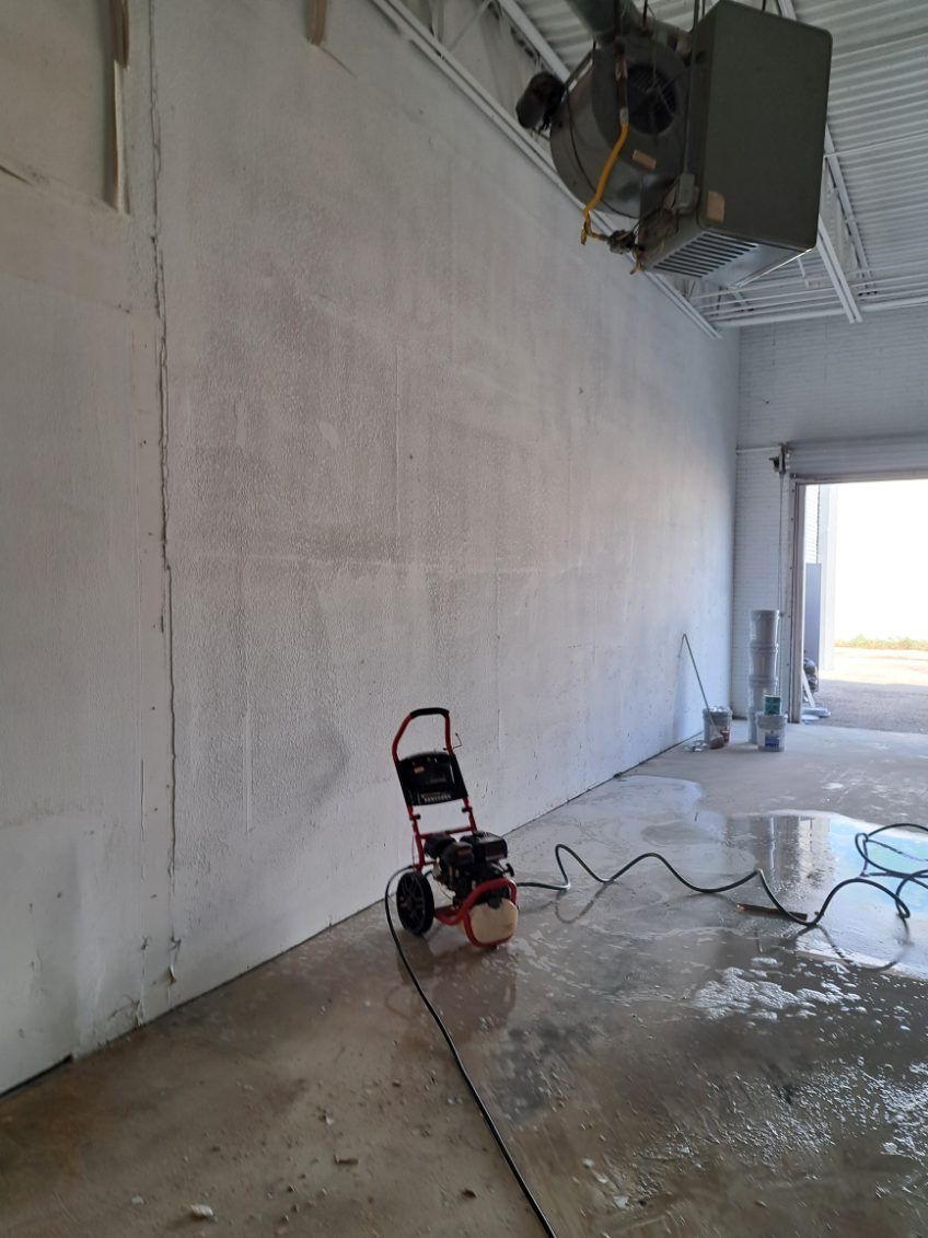 An air compressor is sitting in a large empty room next to a wall.