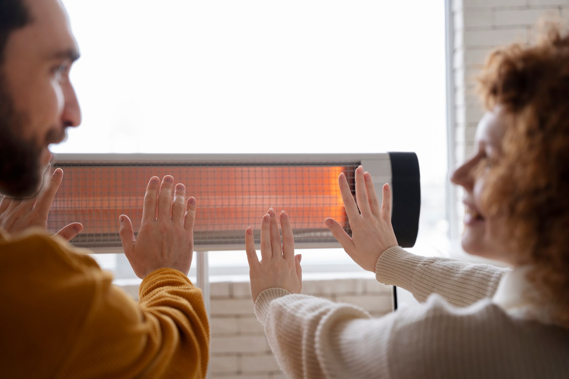 Two people warming their hands in front of an electric space heater