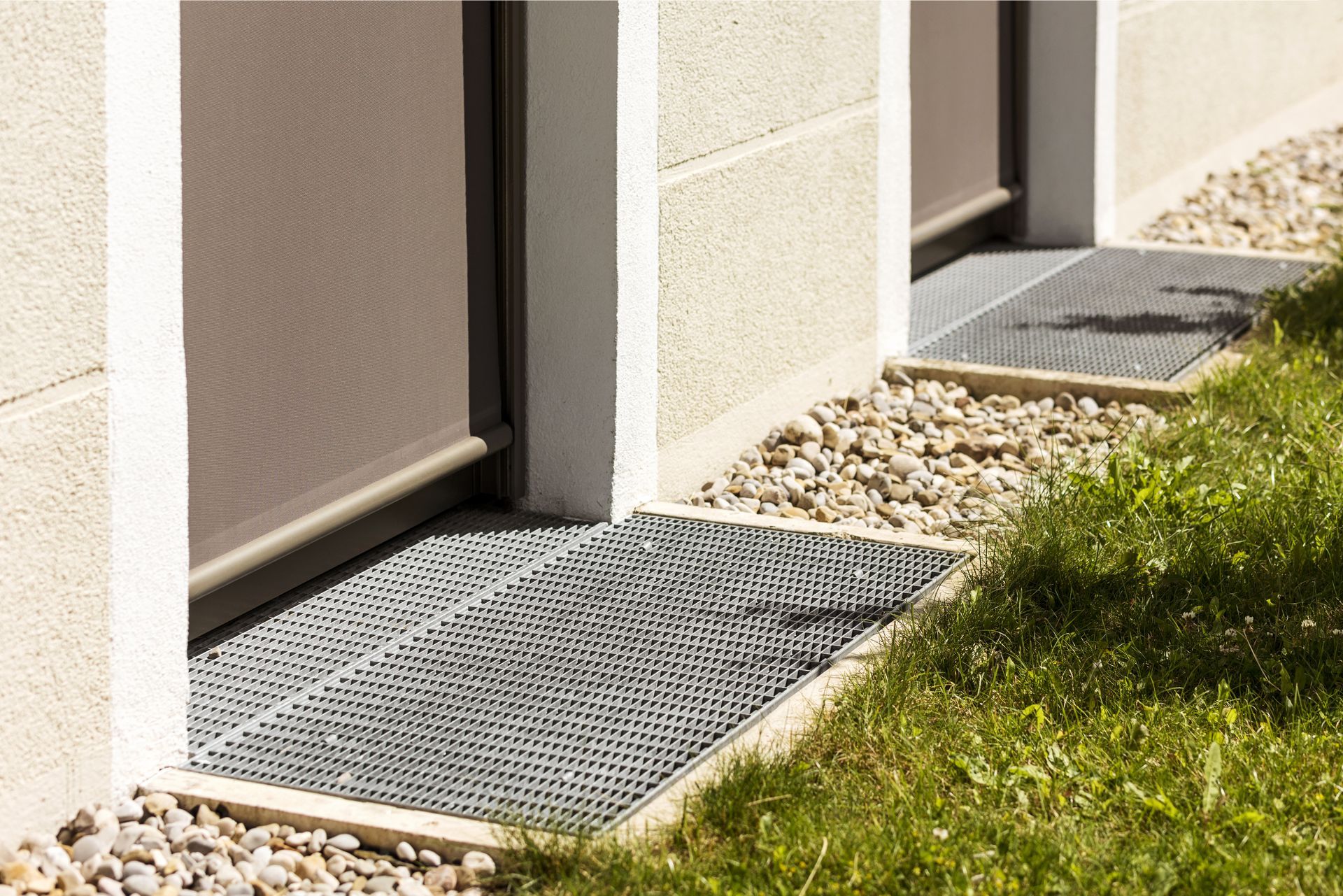 Modern building exterior with metal grate entry mats and gravel landscaping, beside a strip of grass