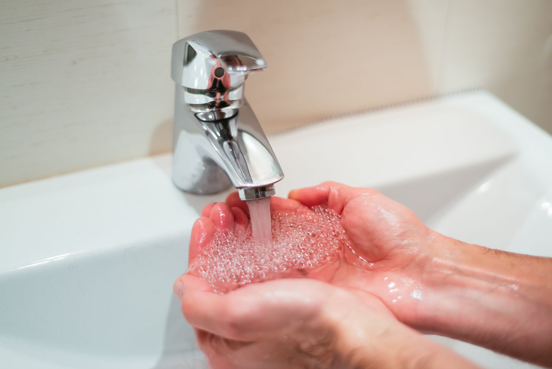 Hands washing under a running chrome faucet with soapy pink lather in a sink