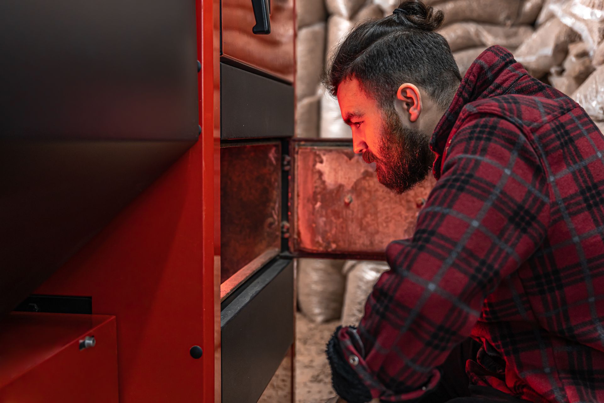 A man in a red plaid shirt inspecting the inside of an industrial furnace or boiler