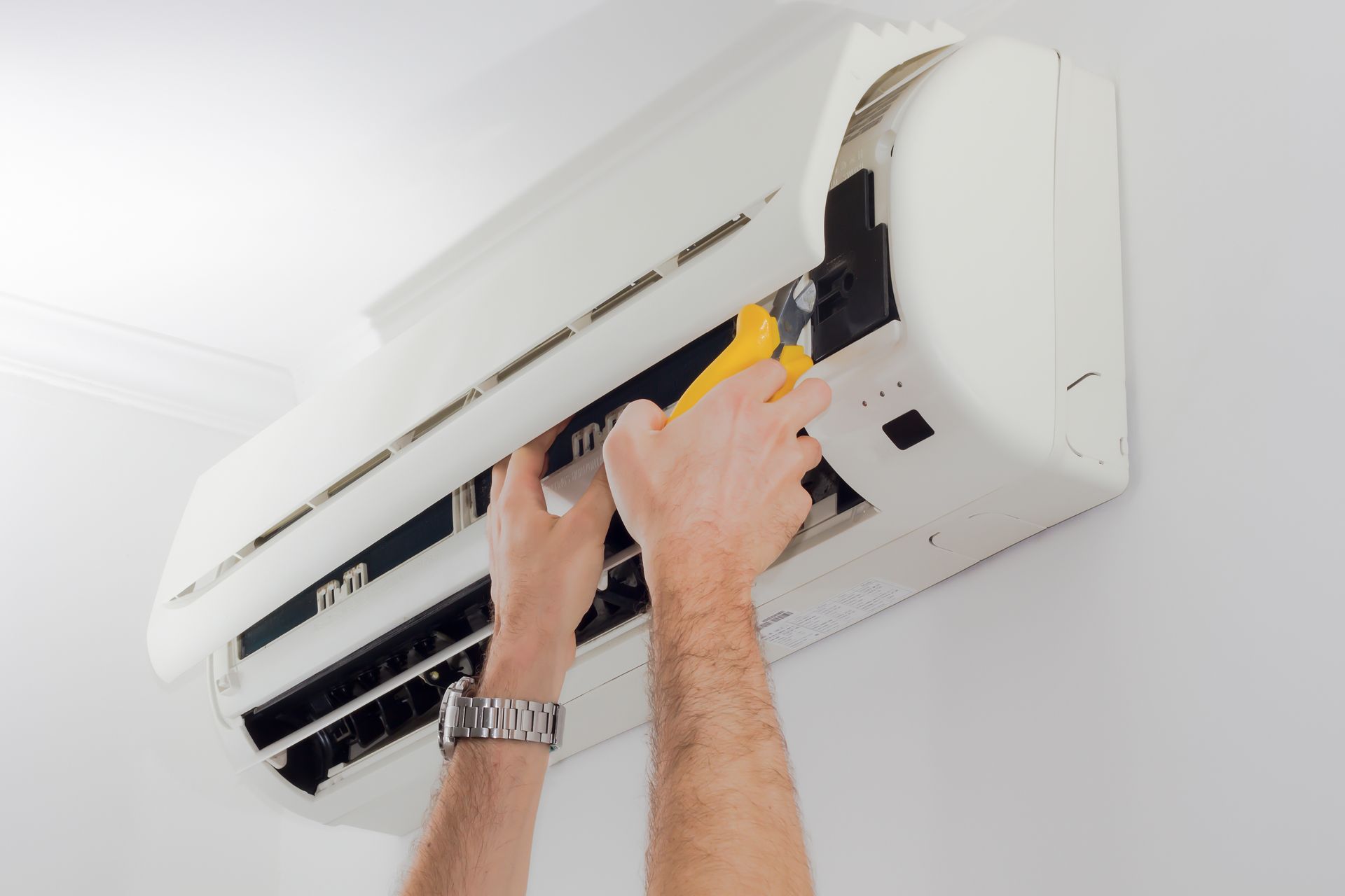 Hands using a yellow tool to service a wall-mounted air conditioner unit.