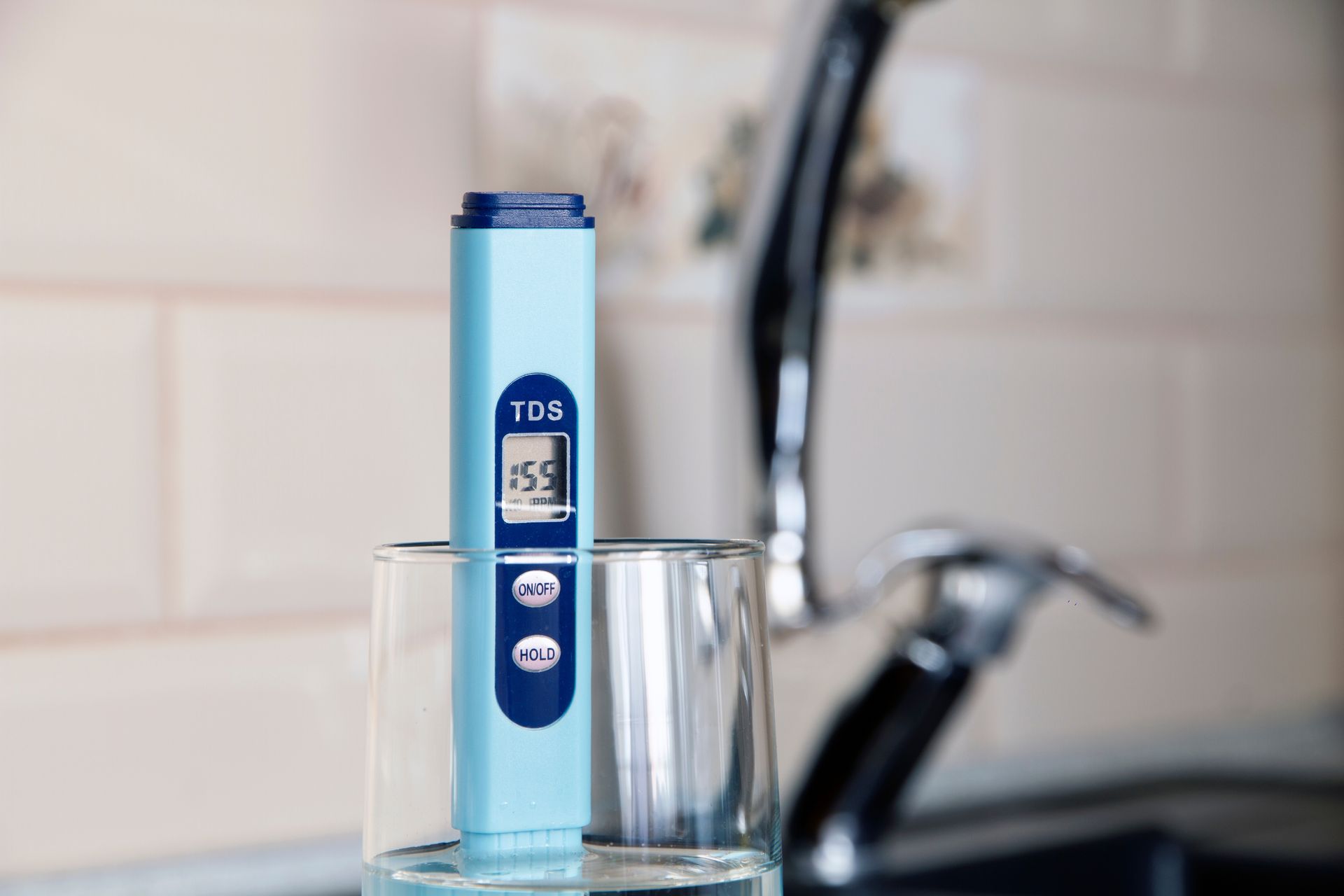 A light blue TDS meter in a glass of water, showing a reading of 35.9, near a kitchen faucet.