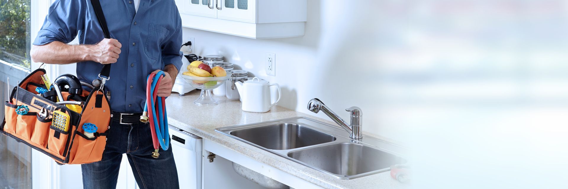 A plumber with a toolbox stands in a kitchen.