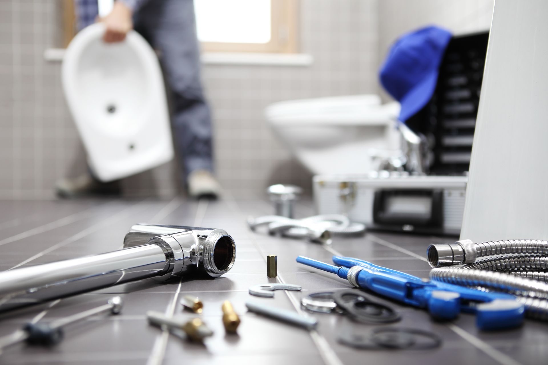 Plumber in a bathroom, tools on the floor. Holding a white bidet, toilet in background.