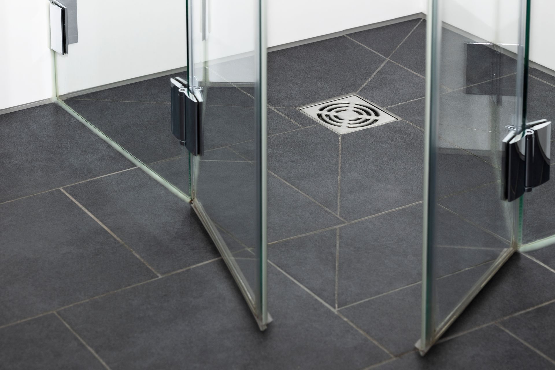 Glass shower enclosure with dark tiled floor and drain.