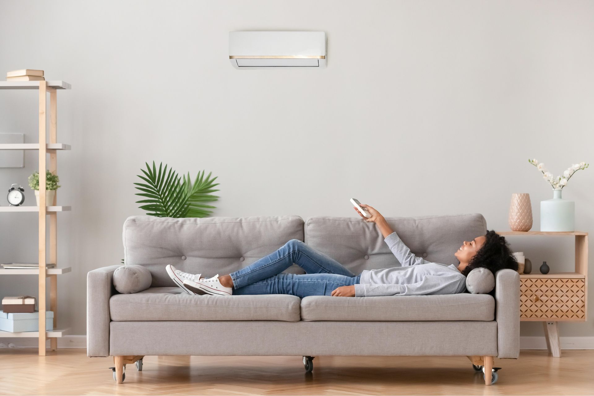 A woman is laying on a couch in a living room holding a remote control.