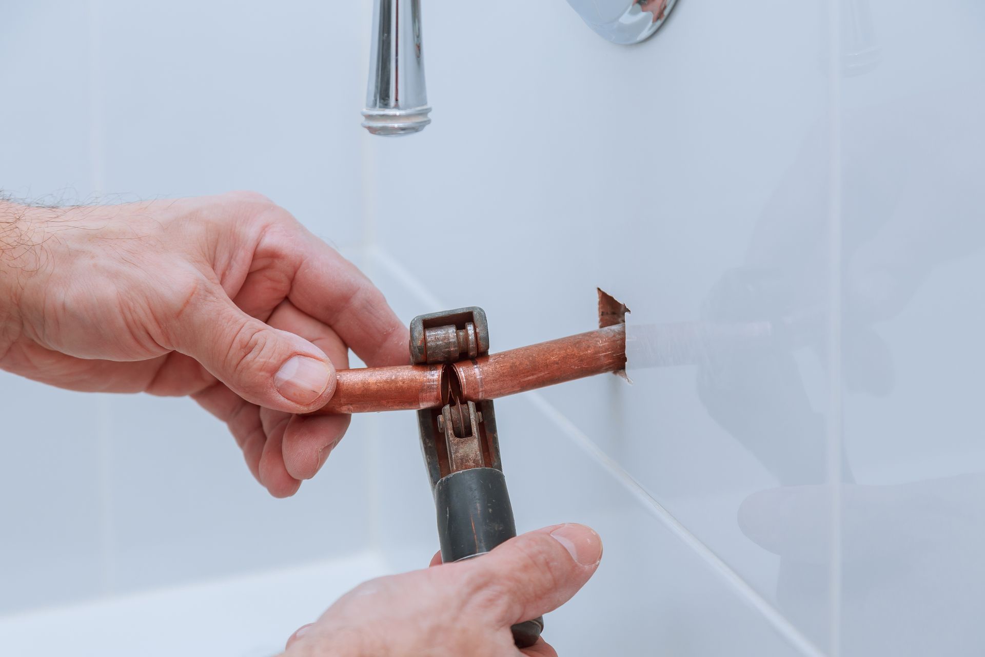 A person is fixing a pipe in a bathroom with a wrench.