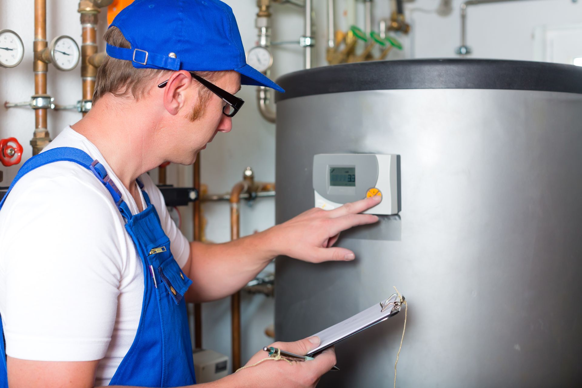 A man is working on a water heater while holding a clipboard.