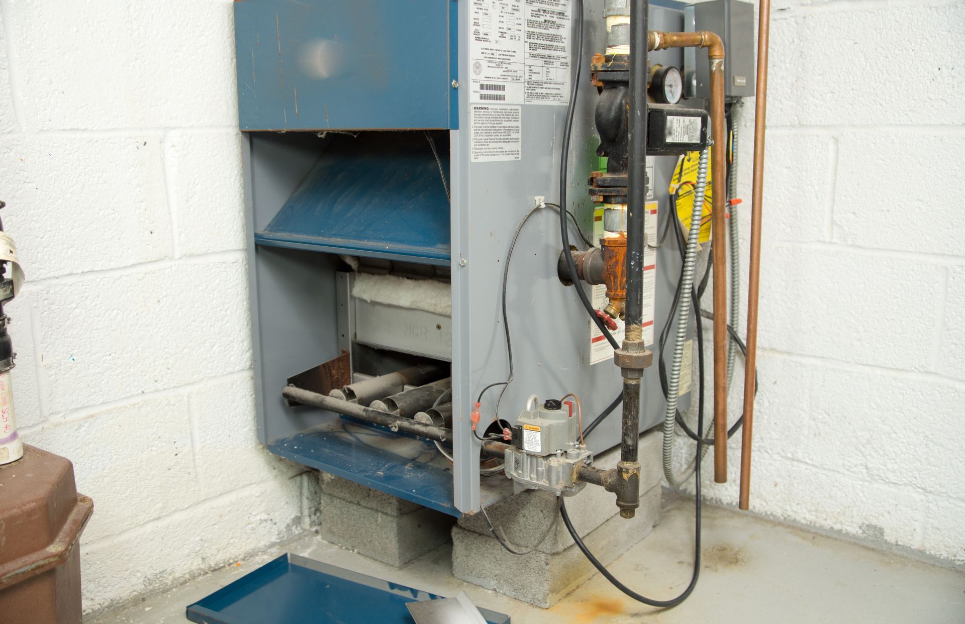 A blue boiler is sitting in a basement next to a brick wall