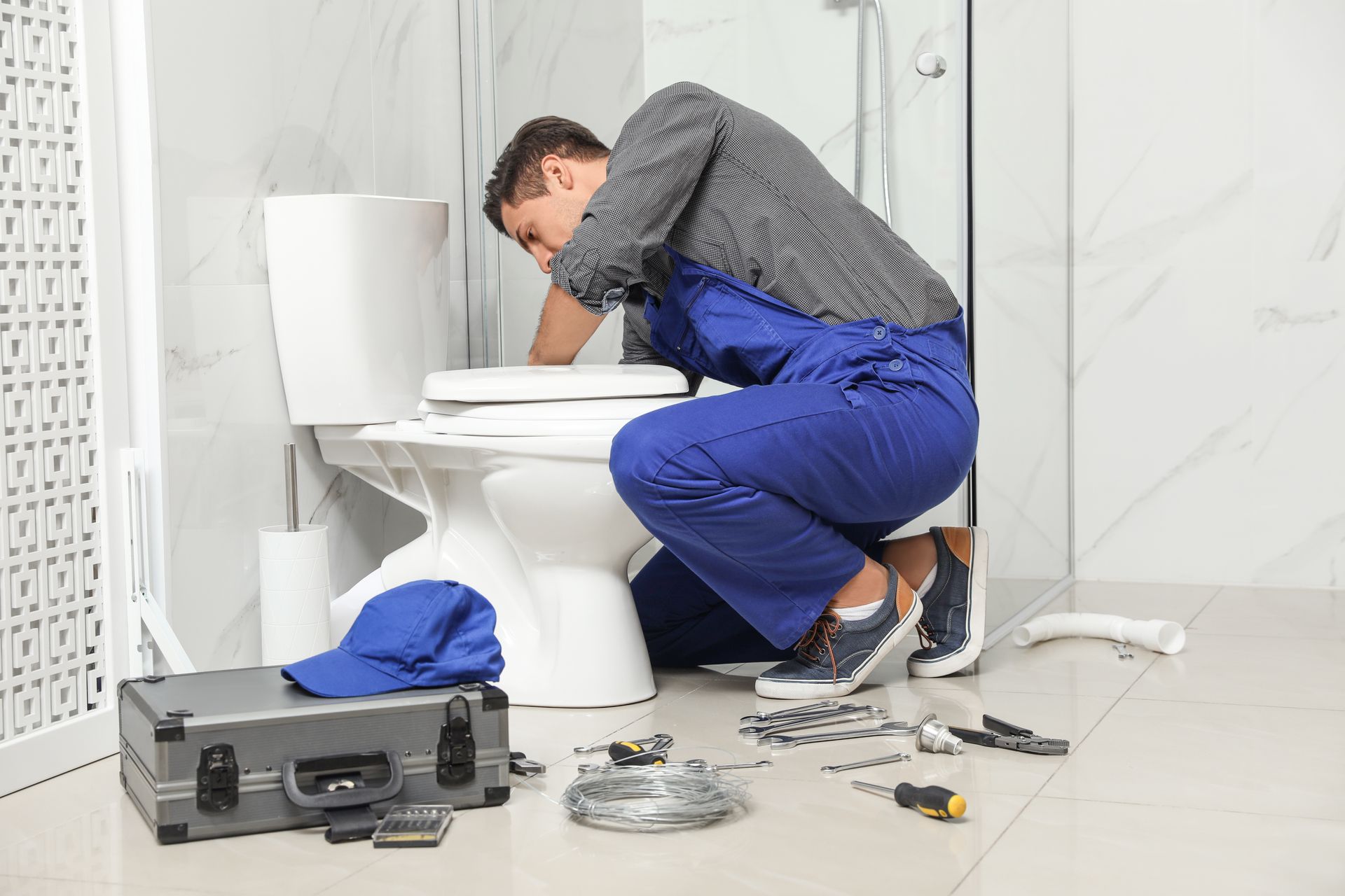 A plumber is kneeling down next to a toilet in a bathroom.