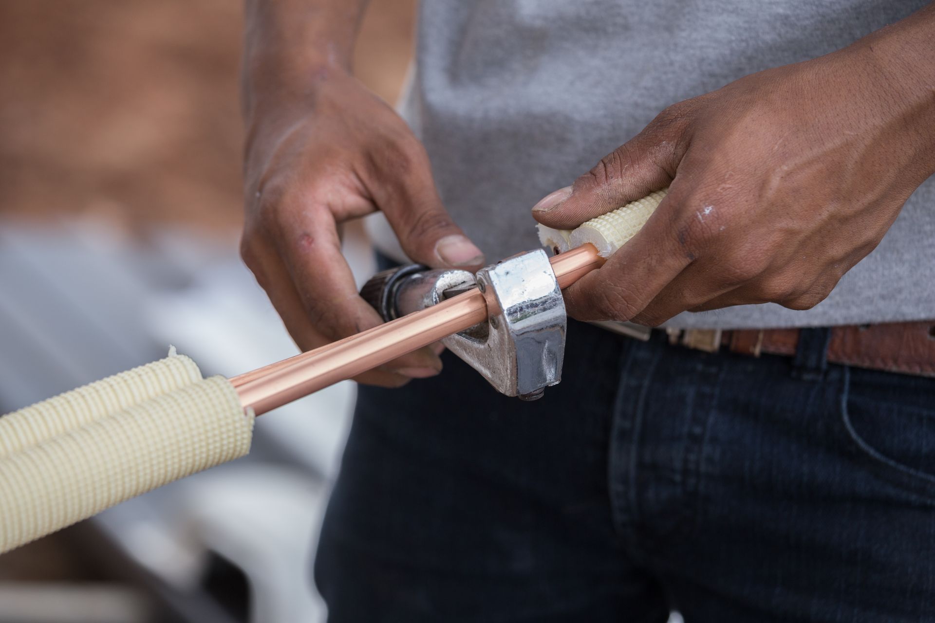 A man is cutting a copper pipe with a pipe cutter.