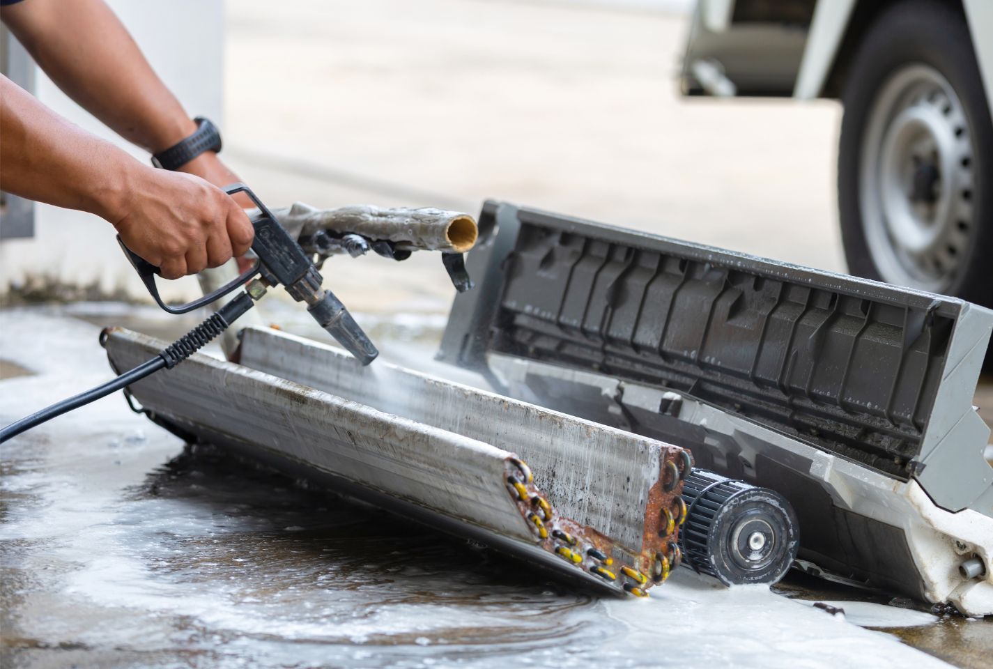 A person is cleaning an air conditioner with a high pressure washer.