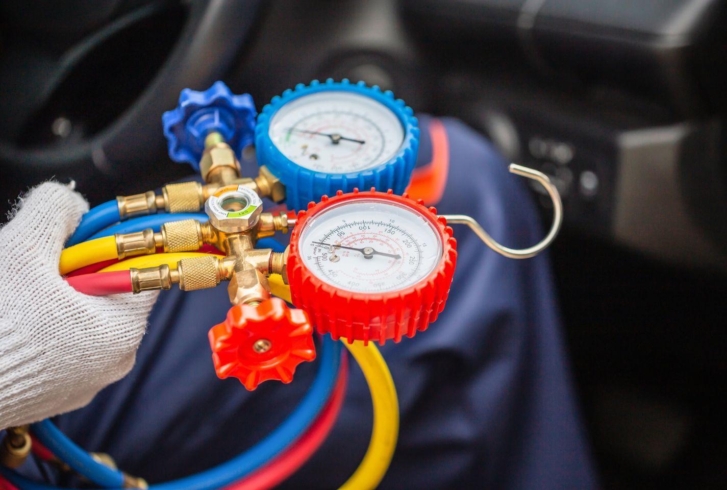 A person is holding a bunch of gauges and hoses in a car.