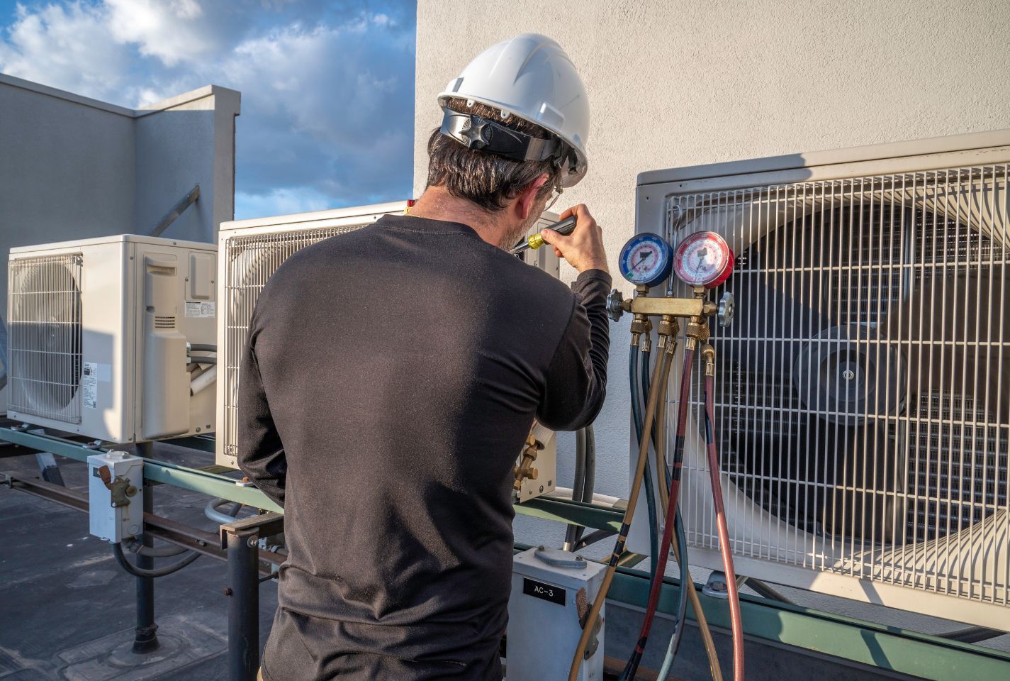 A man is working on an air conditioner on the roof of a building.