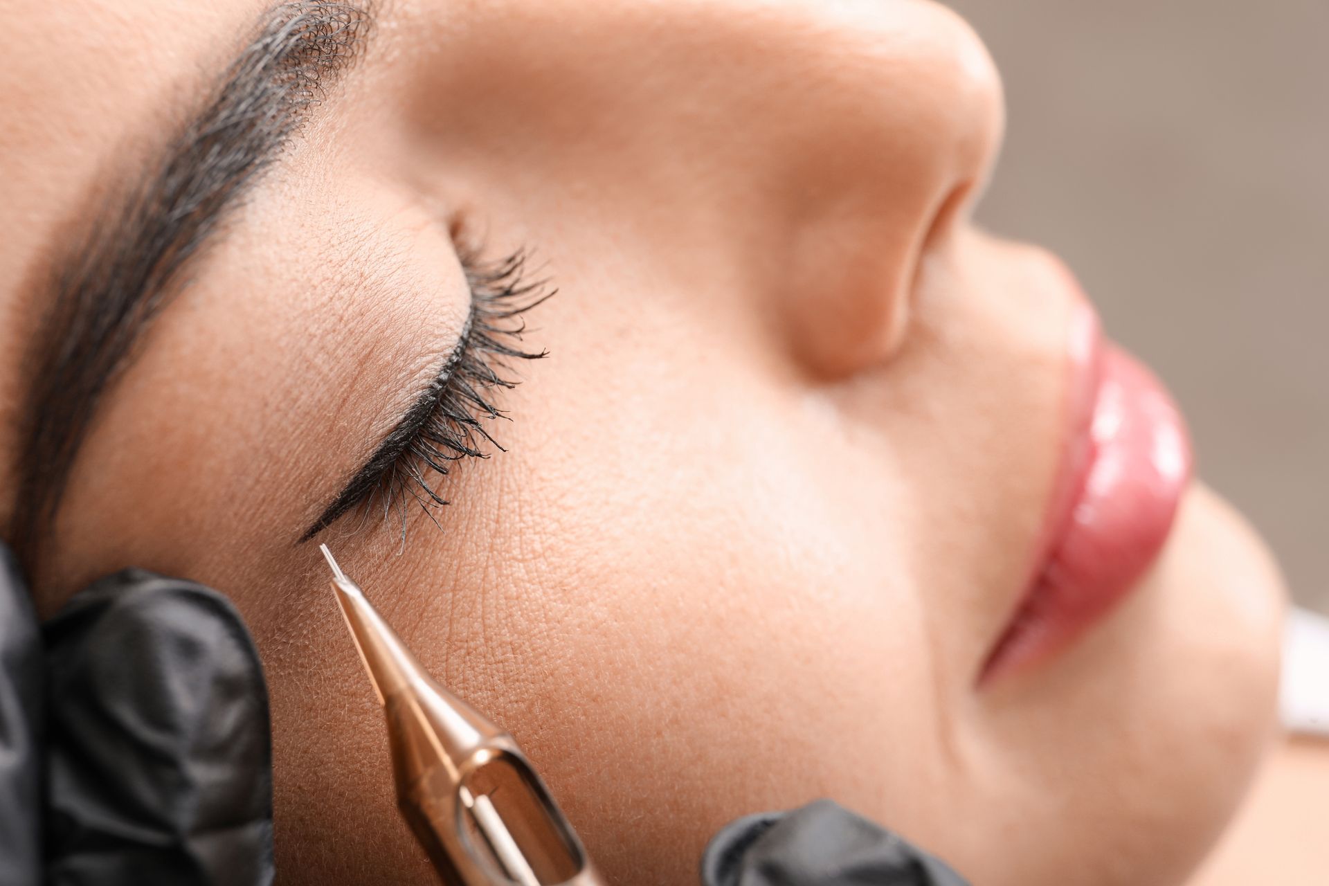 A woman is getting an eyeliner tattoo on her eye.