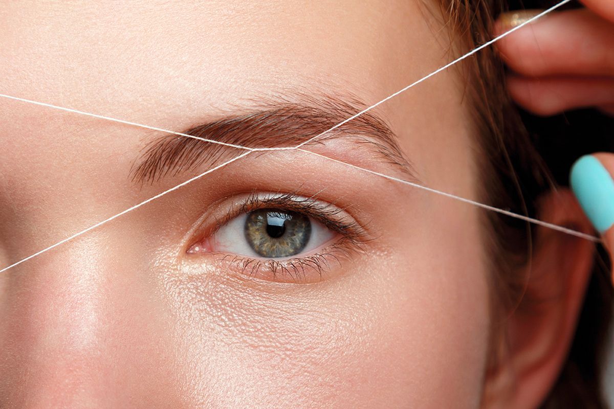 A woman is getting her eyebrows threaded with a string.